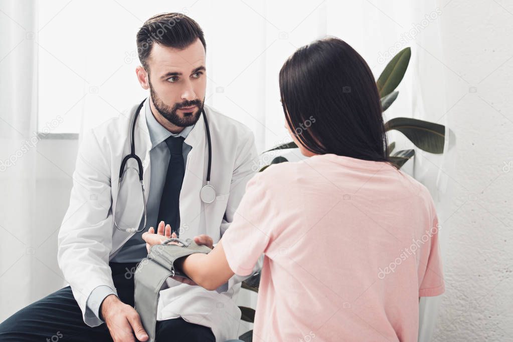 attractive young doctor measuring blood pressure of patient