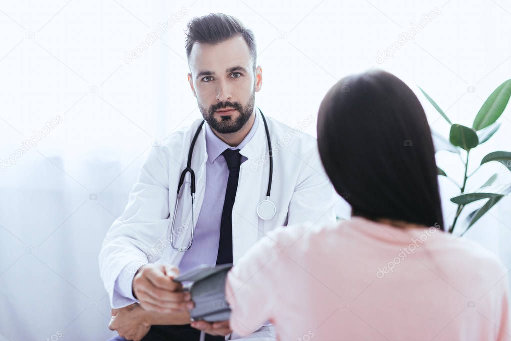 handsome young doctor listening to female patient and looking at camera