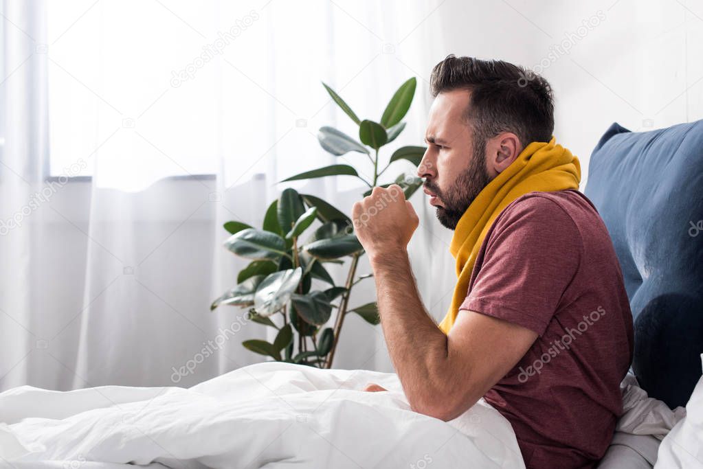 side view of sick young man having cough while sitting in bed