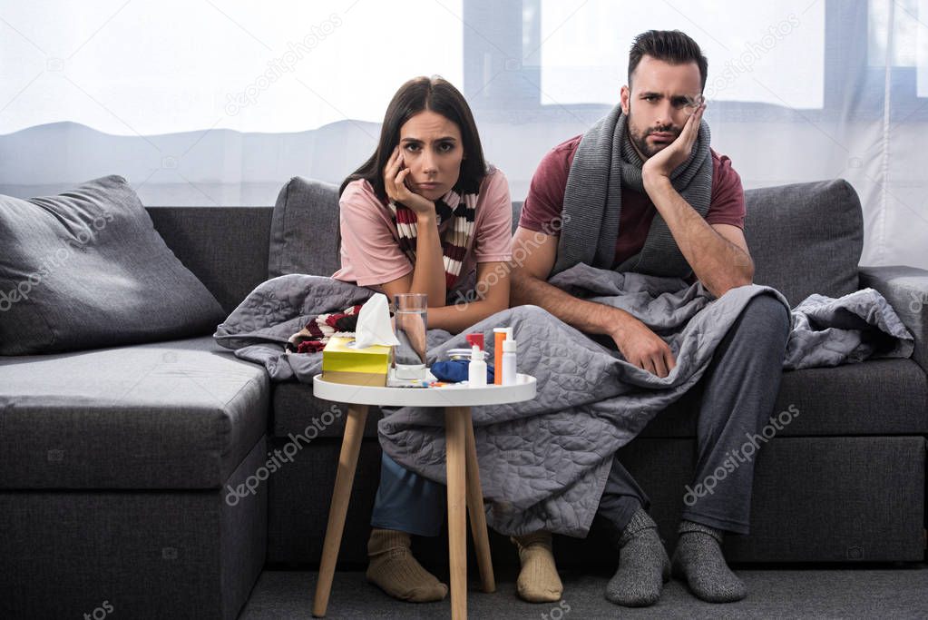 diseased young couple with meds on table sitting together on couch