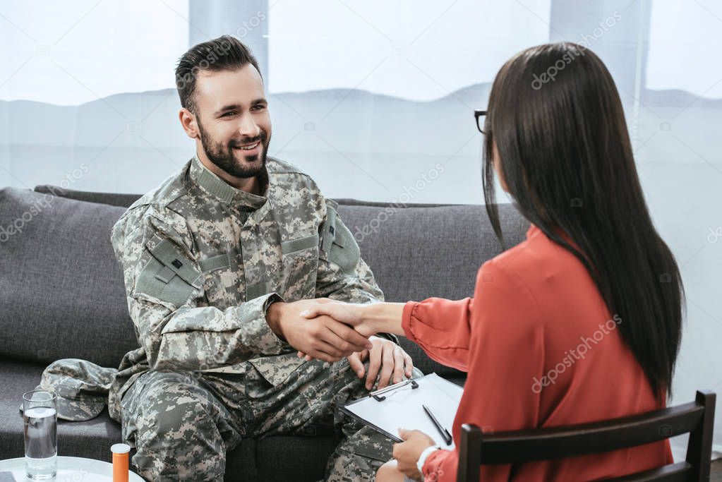 smiling soldier shaking hand of psychiatrist during therapy session