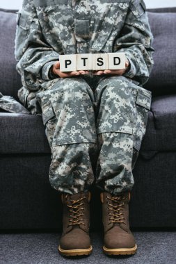 kanepede oturan ve tahta küpleri TSSB işareti ile tutarak askeri üniformalı kadın asker kadeh kırpılmış