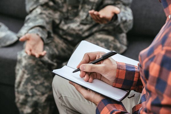cropped shot psychiatrist writing notes during therapy session with female soldier