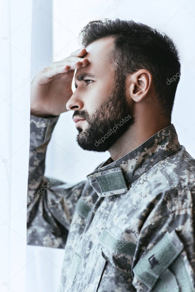 depressed army man in military uniform with post-traumatic stress disorder touching his head and looking away
