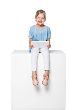 Dijital tablet kullanma ve beyaz küp üzerinde beyaz izole oturan çocuk