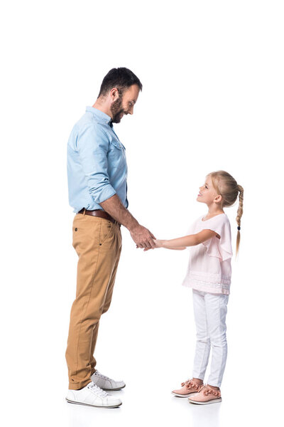 smiling father and daughter holding hands and looking at each other isolated on white