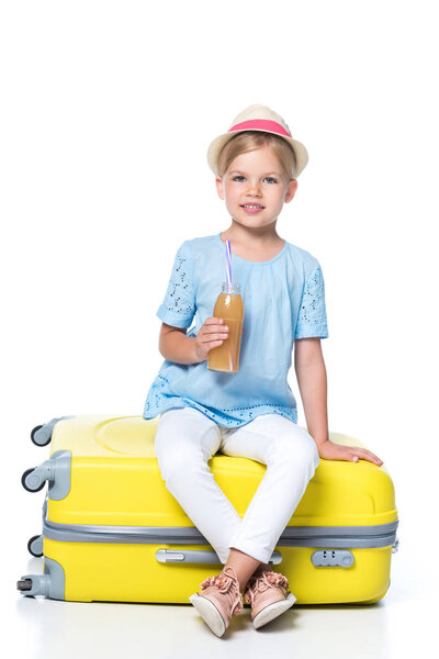 kid with drink sitting on yellow travel bag isolated on white