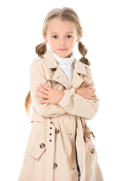 stylish kid posing in beige coat with crossed arms, isolated on white