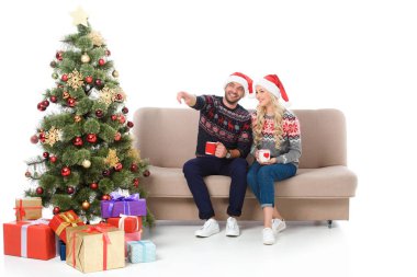 cups ile güzel birkaç kahve ve Divan ile hediyeler, Noel ağacı yakınındaki beyaz izole bir yere işaret eden adam oturuyor