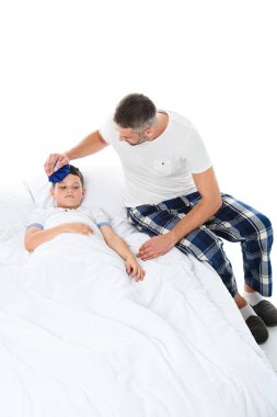 father holding ice pack on head of sick son with temperature lying in bed, isolated on white clipart