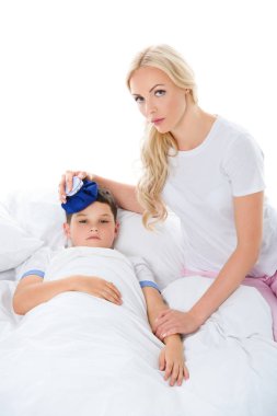 Anne holding buz torbası kafasına beyaz izole yatakta yalan sıcaklık ile hasta oğlu