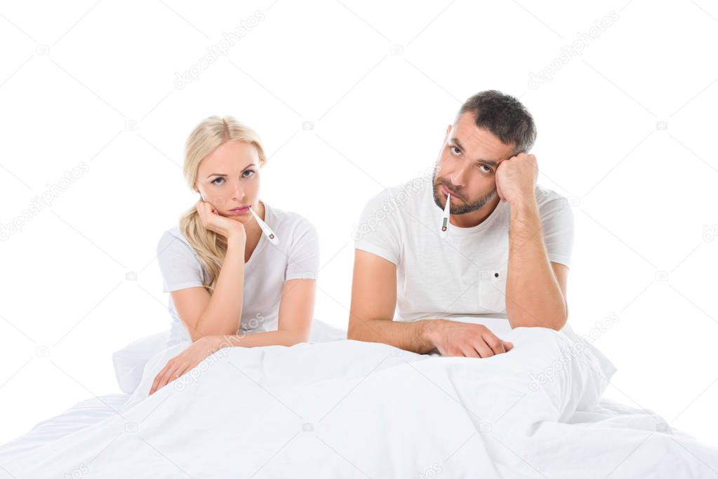 ill couple with electronic thermometers sitting in bed, isolated on white