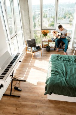 Genç adamın evde akustik gitar çalmak yüksek açılı görünüş
