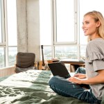 Beautiful smiling woman with laptop sitting on bed at home