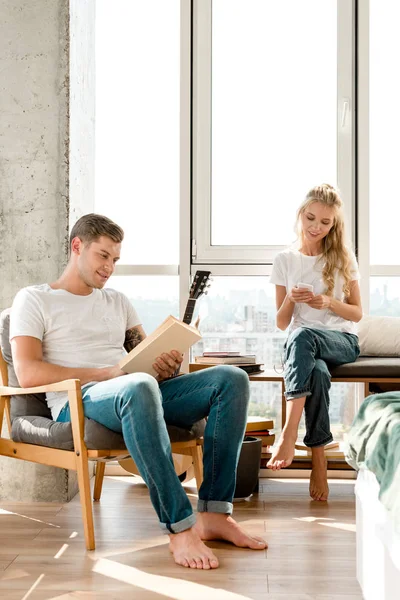 Mujer Usando Smartphone Mientras Novio Leyendo Libro Casa — Foto de stock gratis