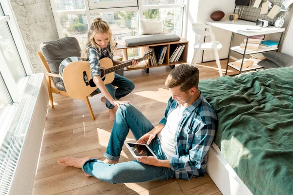Hochblickbild Eines Mannes Mit Digitalem Tablet Während Freundin Hause Akustikgitarre — kostenloses Stockfoto