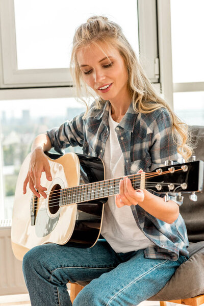 young beautiful woman in casual clothing playing acoustic guitar at home