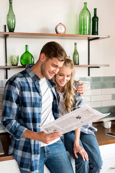 loving couple in casual clothing reading newspaper in kitchen at home