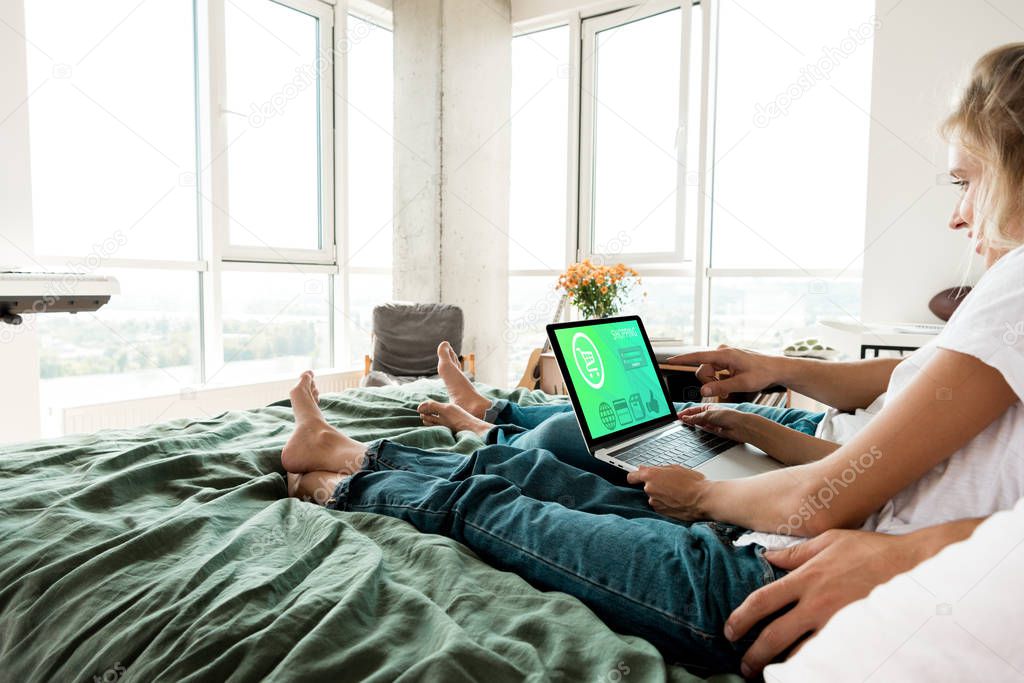 Partial view of couple with digital laptop with shopping lettering on screen resting on bed at home