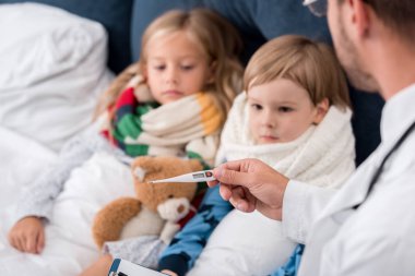 Çocuk doktoru ile yatakta yatan çocuklar sıcaklığını inceleyerek Pano