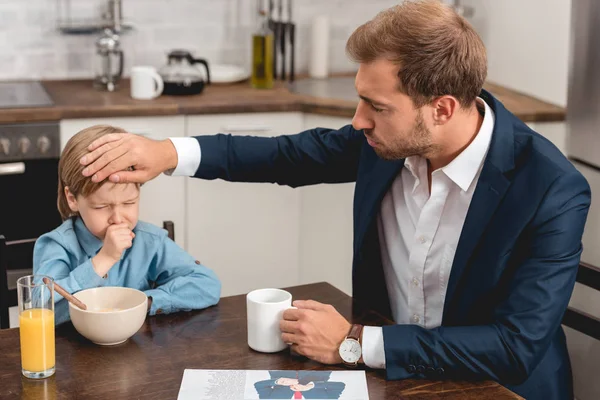 Młody Ojciec Sprawdzanie Temperatury Syna Ręki Podczas Śniadania — Darmowe zdjęcie stockowe