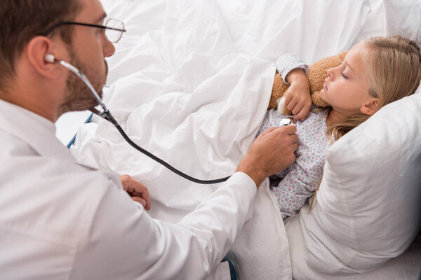 high angle view of pediatrician litening childs breath with stethoscope while she lying in bed