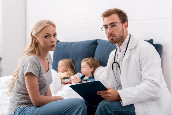 Pediatra Madre Mirando Cámara Mientras Los Niños Enfermos Yacen Cama —  Fotos de Stock