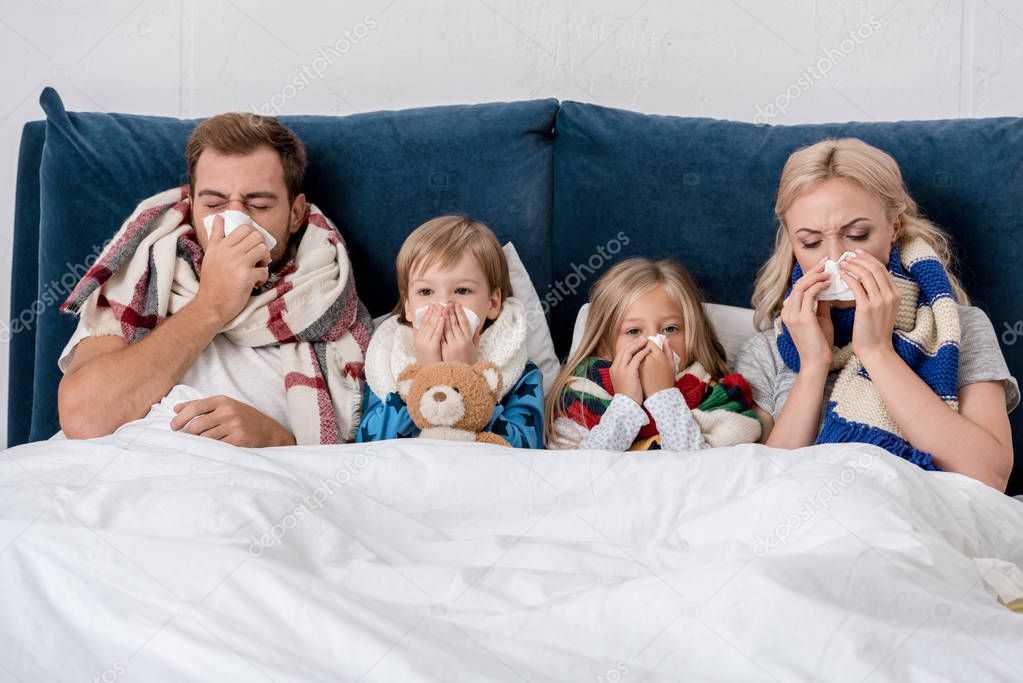 sick young family blowing noses with napkins together while lying in bed