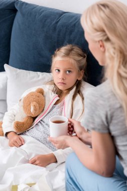 hasta kızı yatakta ısınma çay veren genç anne