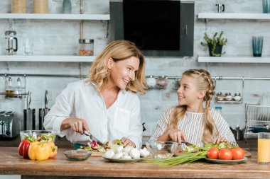 mutlu yetişkin anne ve küçük kızı birlikte marul salata için kesme ve evde sohbet