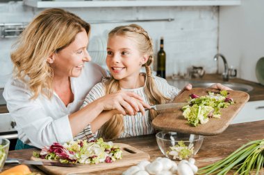 mutlu yetişkin anne ve küçük kızı evde birlikte salata yapma
