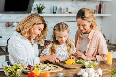 Annem ve anneannem evde küçük bir çocuk kesme sebze salatası için konsantre