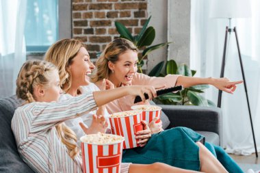 Annem ve büyükannem kova patlamış mısır ile kanepe evde film izlerken ve ekranında işaret ile heyecanlı çocuk