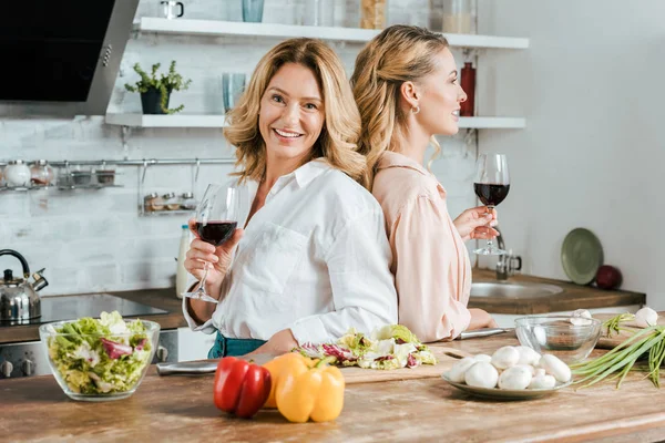 快乐成熟的母亲和成年的女儿用红酒杯站在后面的厨房 — 图库照片