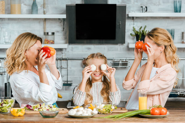 adorable little child covering eyes with food with mother and grandmother at home while cooking