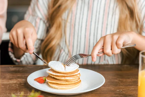 cropped shot of child eating pancakes with strawberry
