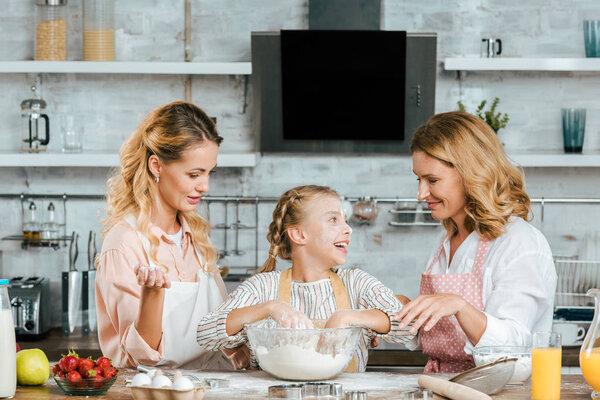 happy little child preparing dough with mother and grandmother at home