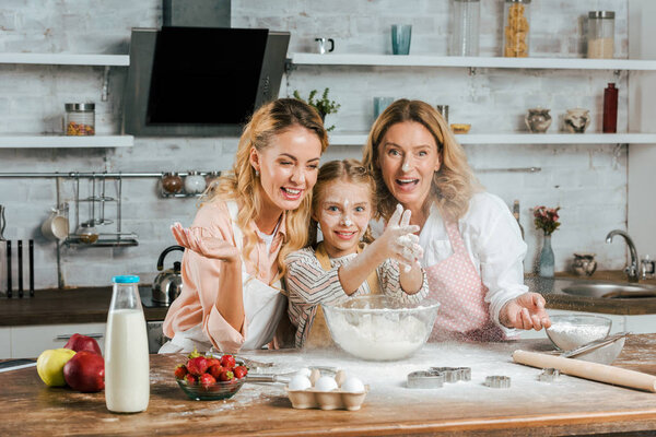 happy child clapping hands with flour while cooking with mother and grandmother at home