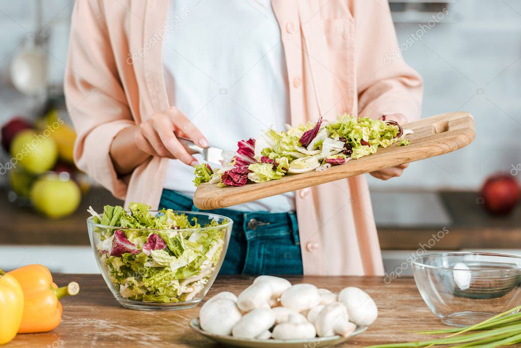 cropped shot of woman pouring cut lettuce into bowl from cutting board