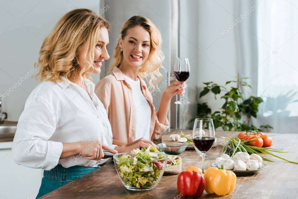 happy mature mother and adult daughter making salad together at kitchen