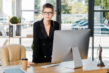 bilgisayar ve ofis kamerada bakarak masada eğilerek bardaklarda çekici iş kadını