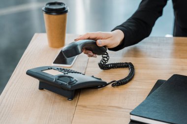 cropped image of businesswoman taking handset of stationary telephone in office clipart