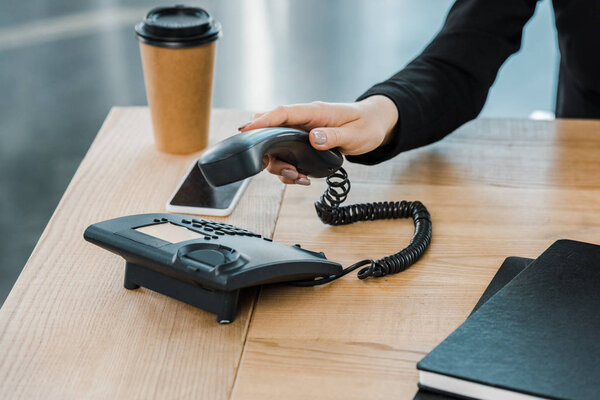 cropped image of businesswoman taking handset of stationary telephone in office