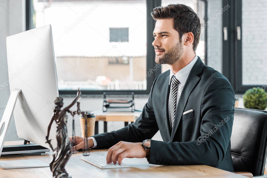 handsome lawyer working with computer at table in office, themis statue on tabletop