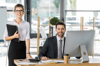 smiling businessman and businesswoman looking at camera in office clipart