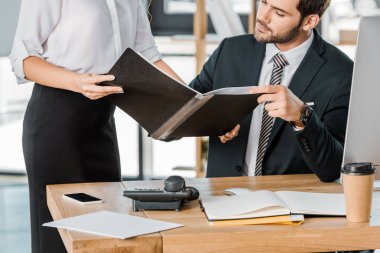 cropped image of businesswoman showing folder with documents to businessman in office clipart