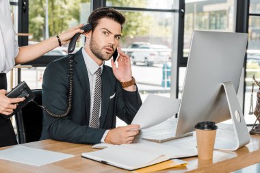 şok işadamı akıllı telefon ve cep telefonu kulağına yakınındaki sabit telefon tutarak Sekreter tarafından söz