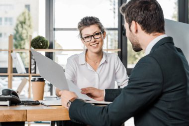 smiling businesswoman and business partner with papers discussing work at workplace in office