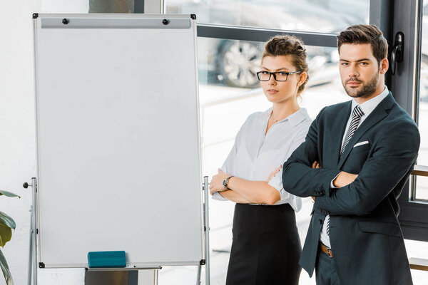 portrait of young business colleagues with arms crossed standing at empty white board in office