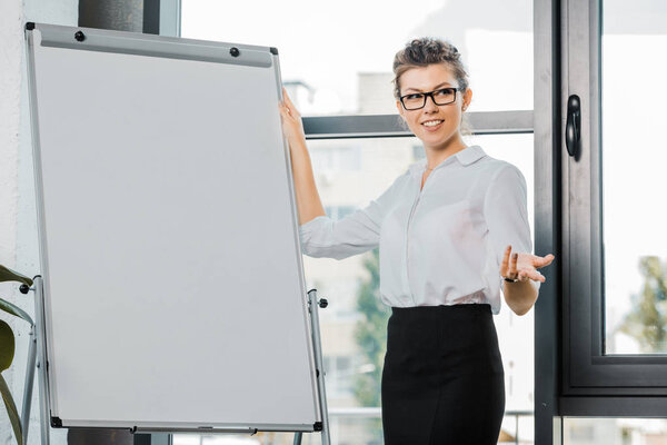 portrait of smiling businesswoman in eyeglasses standing at white board in office